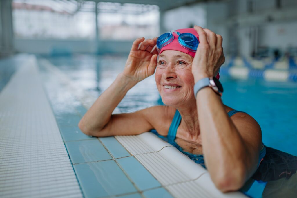 Happy senior woman in swimming pool, leaning on edge